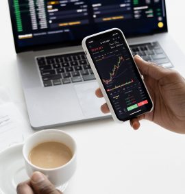 LearnOnline Self-study Economics A level Hand holding phone with finance market data with laptop in the background