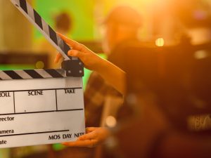 Film Studies A level. Hands holding empty clapperboard with film equipment and people blurred in background