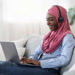 person smiling wearing a headset looking at a laptop