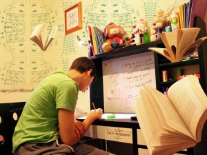 LearnOnline Exams - 16-18 year old sat at desk with writing on wall and books flying around