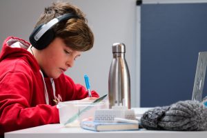 LearnOnline news article - what is an IGCSE? LearnOnline news article - what is an IGCSE? 12-14 year old boy in red jumper sat at desk studying with headphones