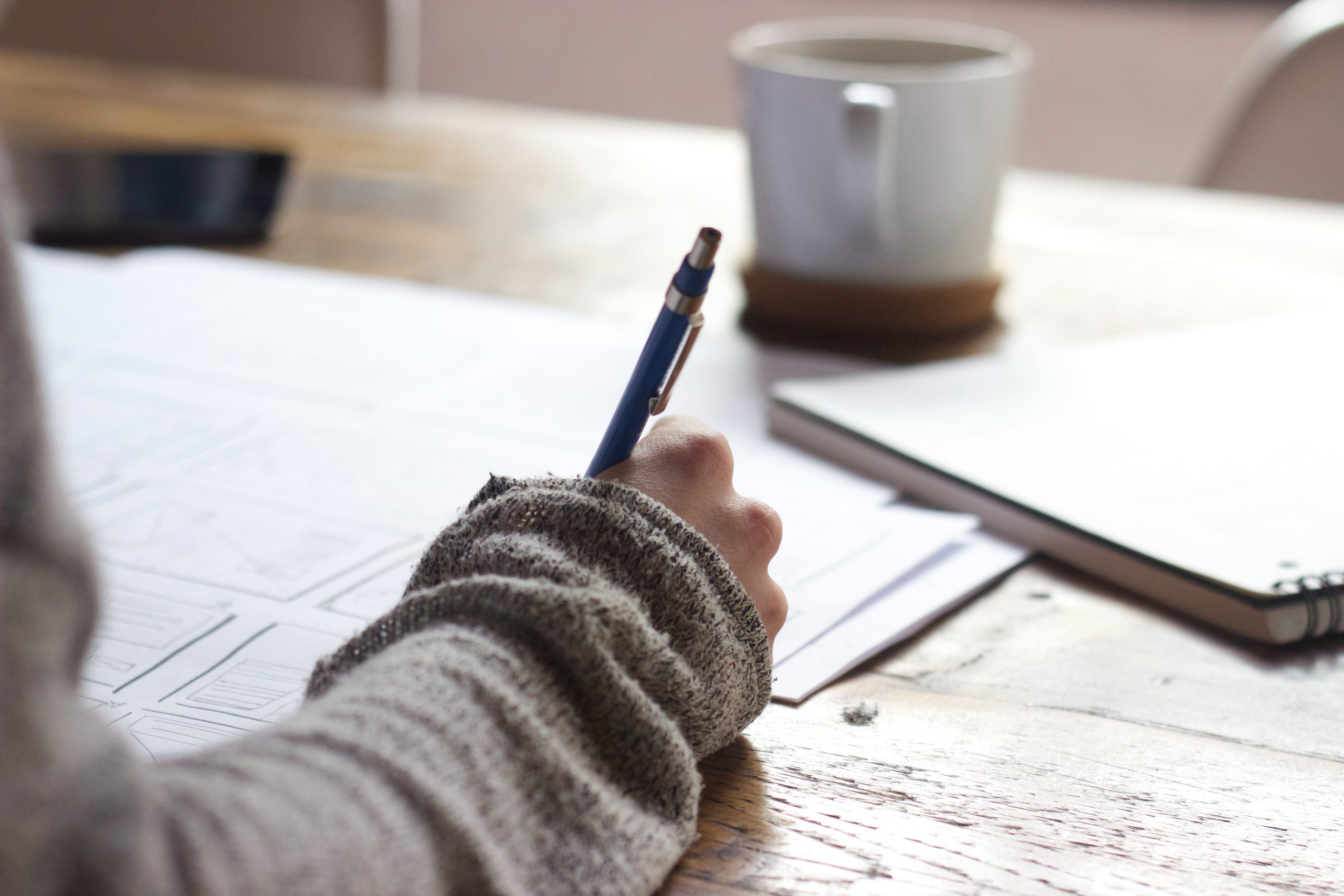 LearnOnline Home Education - qualifications hand with pen writing on paper with cup in background