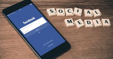 Social Media news article Mobile phone with Facebook icon on the screen with Scrabble letters spelling out 'social media'