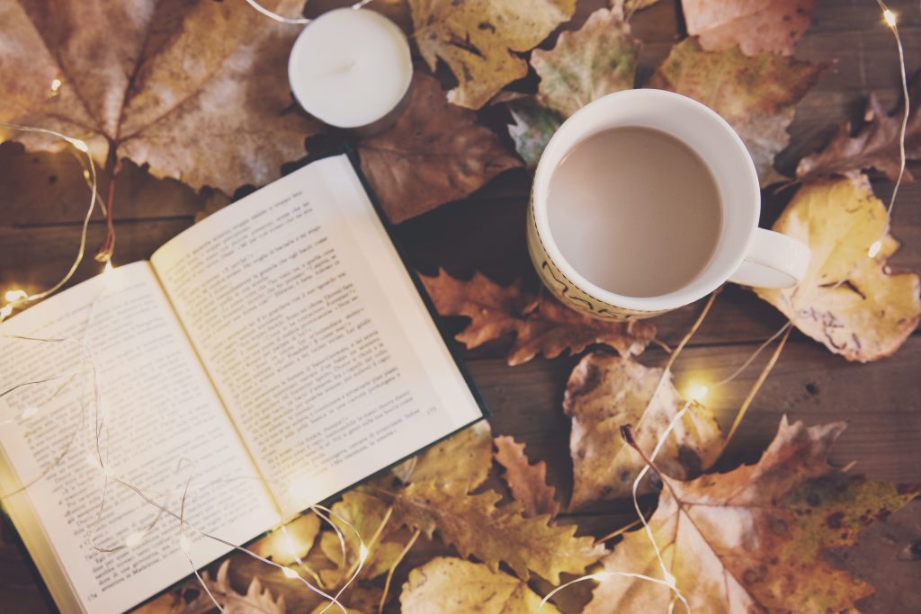 Enrol with us at any time news article Book, cup of tea and candle on a table with Autumnal leaves